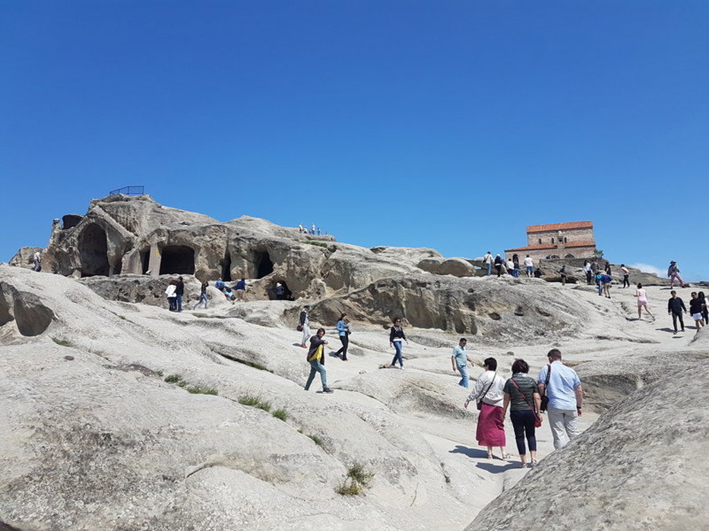 Bezoekers bij de rotsstad Uplistsikhe in Georgië met uitgehouwen grotten en een kerk op de heuveltop.