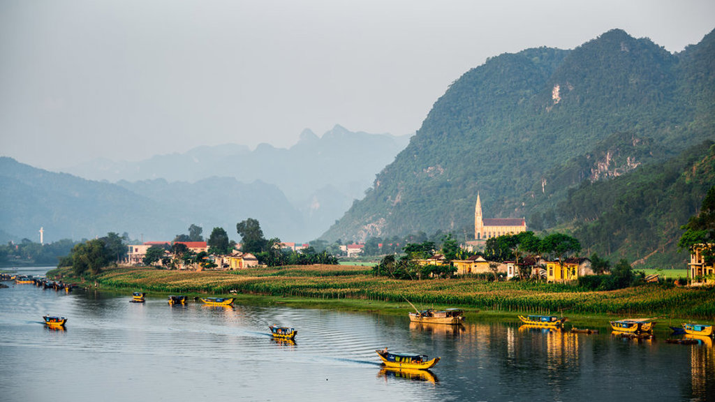 Karstbergen en rivier met kleurrijke bootjes bij een dorp in Vietnam tijdens een groepsrondreis.