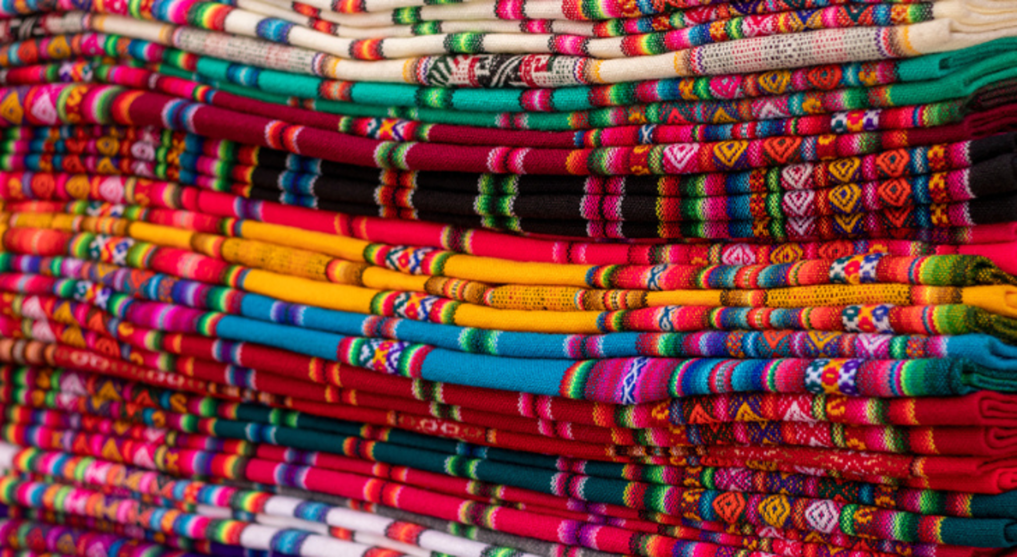 Stapels kleurrijke, geweven textiel met traditionele patronen op een markt in Bolivia.