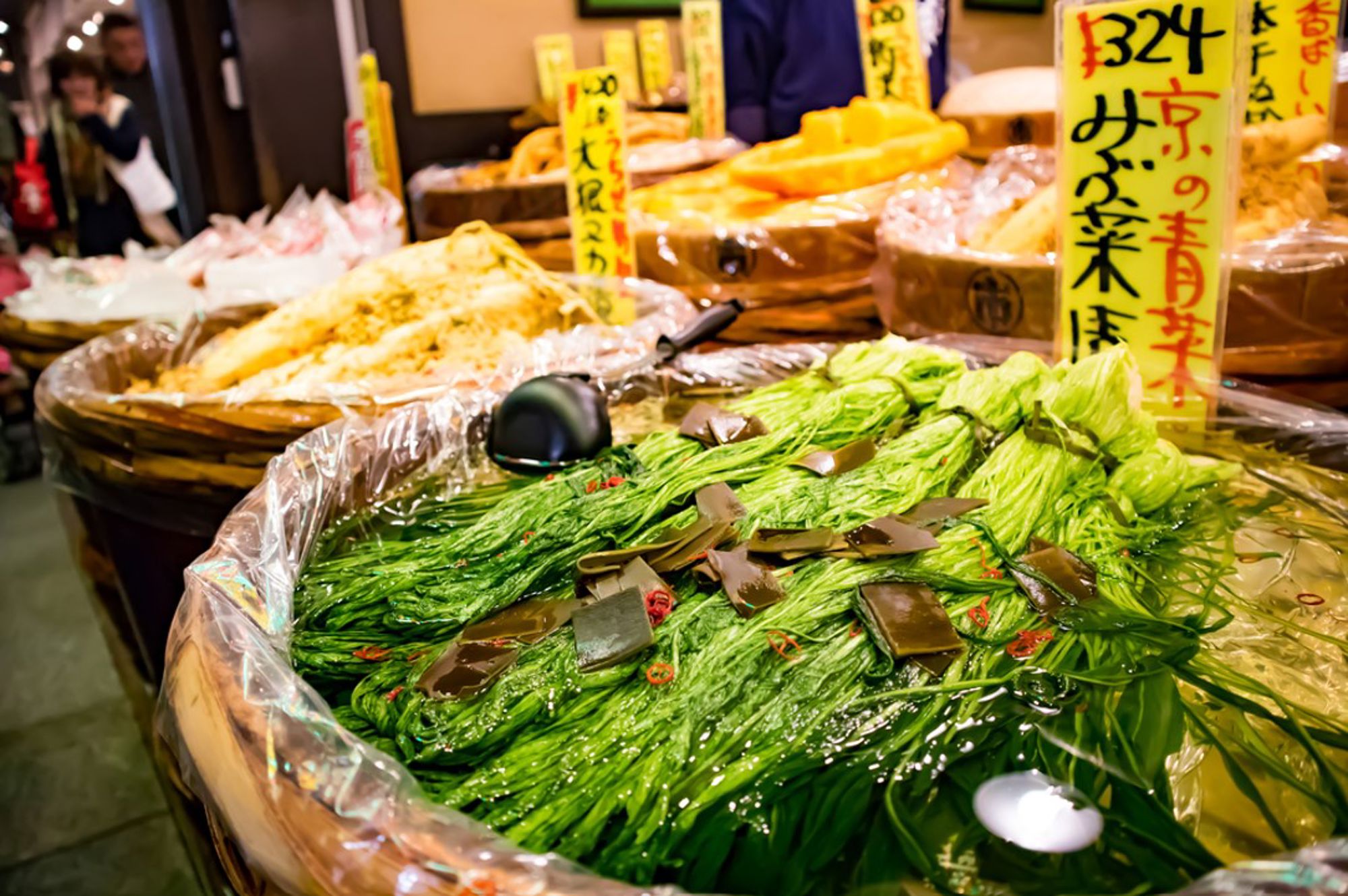Japanse markt met ingelegde groenten en zeewier in grote houten vaten met prijsetiketten.