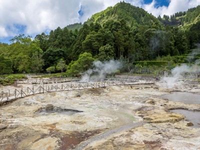Stoompluimen bij warmwaterbronnen in Furnas op São Miguel, Azoren, met wandelpaden en groene heuvels.