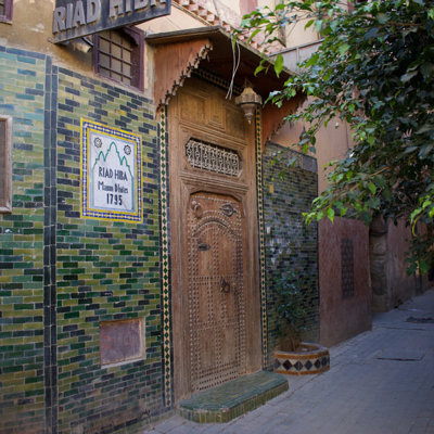 Ingang van een riad met groene mozaïektegels en houten deur in een smalle steeg in Marokko.