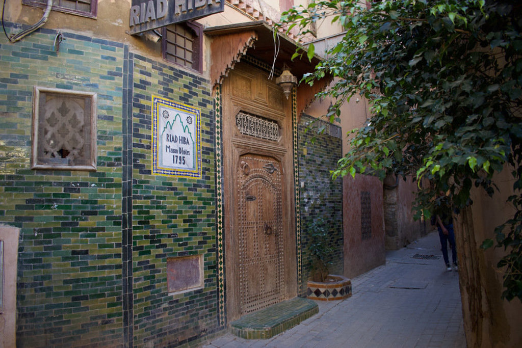 Ingang van een riad met groene mozaïektegels en houten deur in een smalle steeg in Marokko.