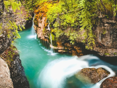 Waterval in een rotsachtige kloof met turquoise rivier, omringd door groen bos in Canada.