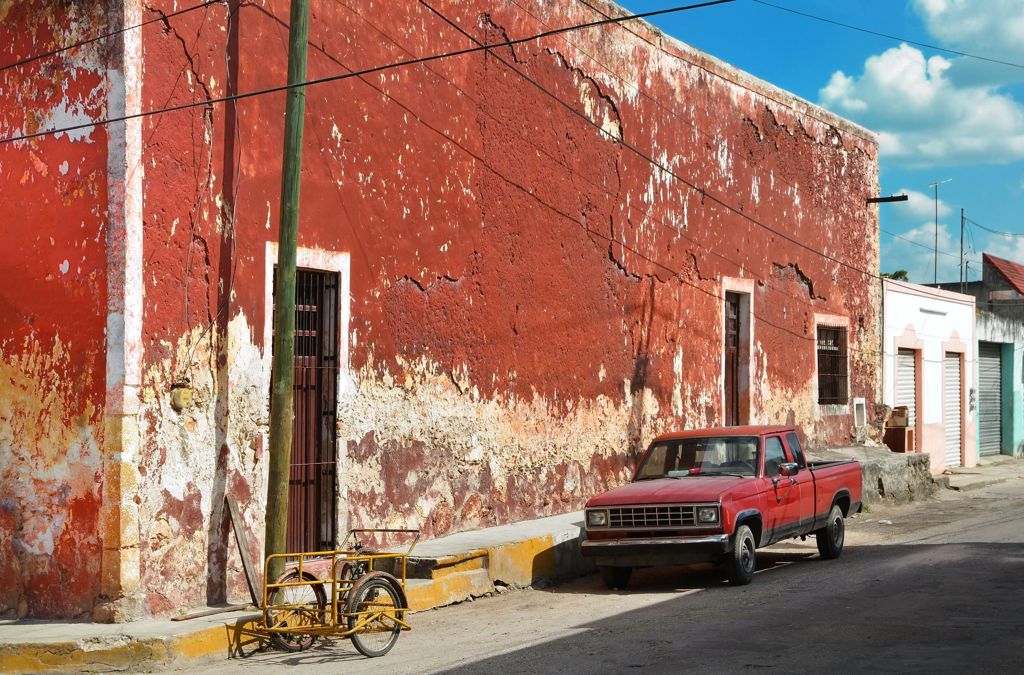 Rode pick-up en gele kar op straat langs verweerde gevel in Mexico, tijdens familiereis langs hoogtepunten.