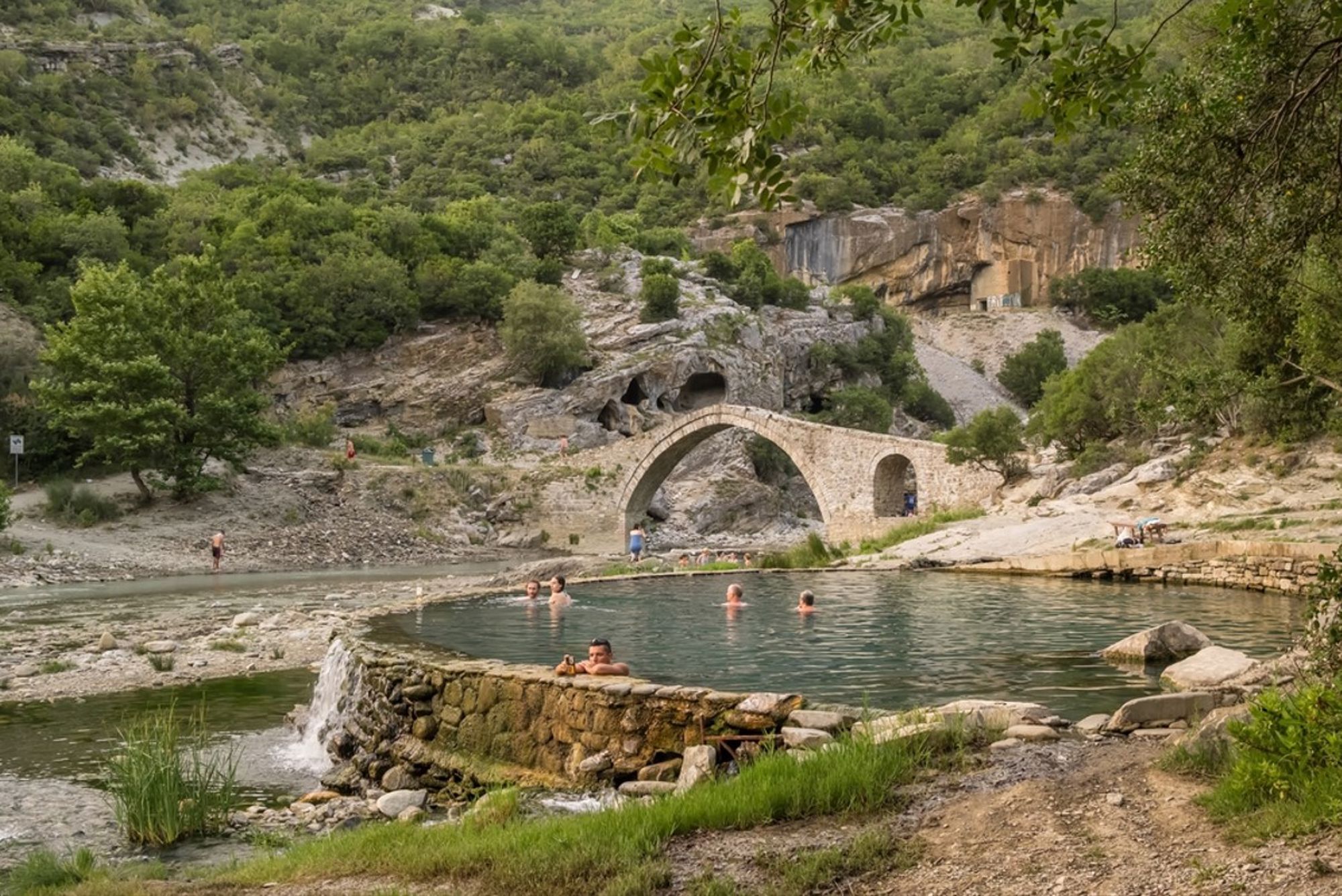 Natuurlijke zwempoel bij de Benja Thermal Baths met Ottomaanse stenen brug in Albanië.