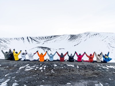 Groep reizigers met opgeheven armen op een bergkam met uitzicht op besneeuwde bergen in Noord-IJsland.