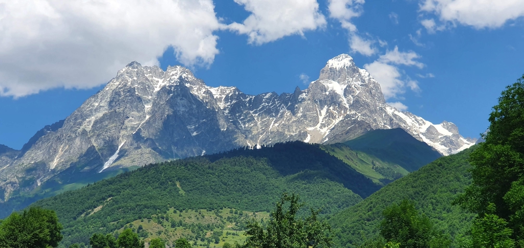 Berglandschap in Georgië met besneeuwde Kaukasus-toppen boven groene heuvels en een blauwe lucht.
