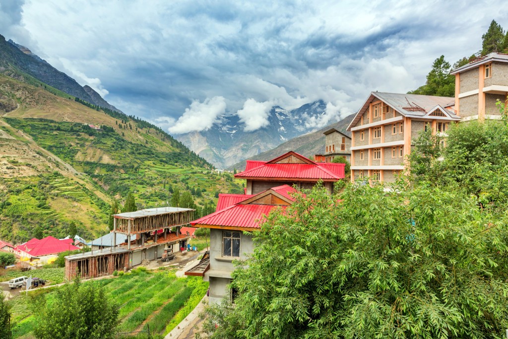 Bergdorp in Spiti of Ladakh met rode daken en groene valleien, met besneeuwde toppen onder dreigende wolken.