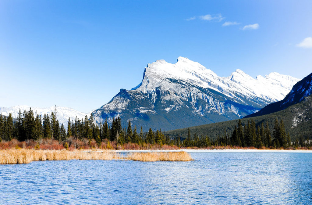 Besneeuwde bergtoppen in de Canadese Rockies bij een helderblauw meer en dennenbos.