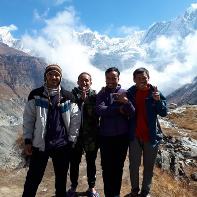 Dragers en gidsen poseren bij Annapurna Basecamp met besneeuwde Himalayapieken op de achtergrond.
