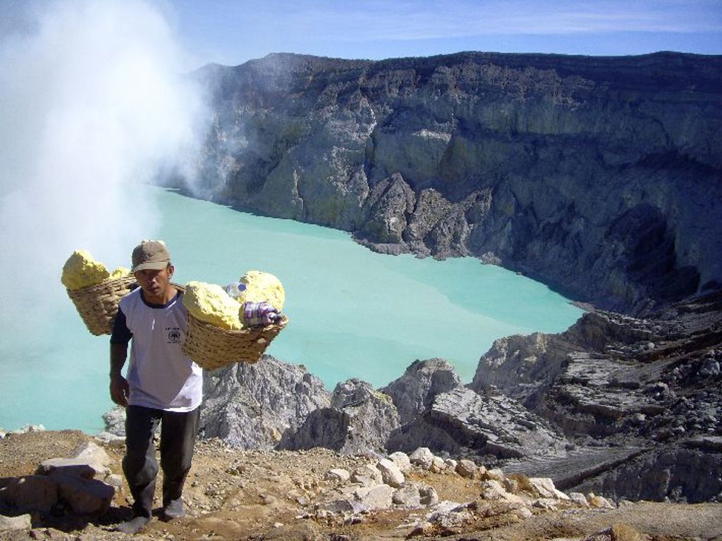 Zwaveldrager bij de Ijen-vulkaan op Java met turquoise kratermeer en rookpluimen.