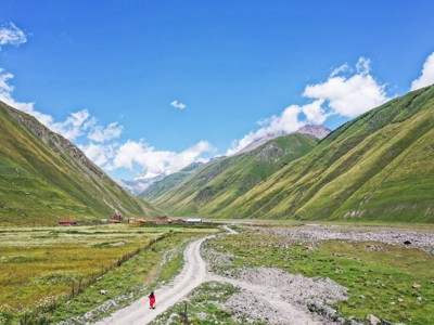 Bergvallei in Georgië met kronkelende zandweg en kleine nederzetting tussen groene hellingen.