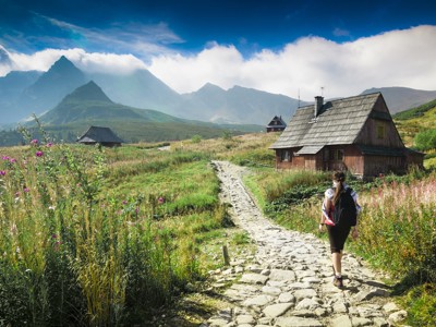 Wandelaar op bergpad langs houten berghut met uitzicht op het Tatragebergte in Polen.
