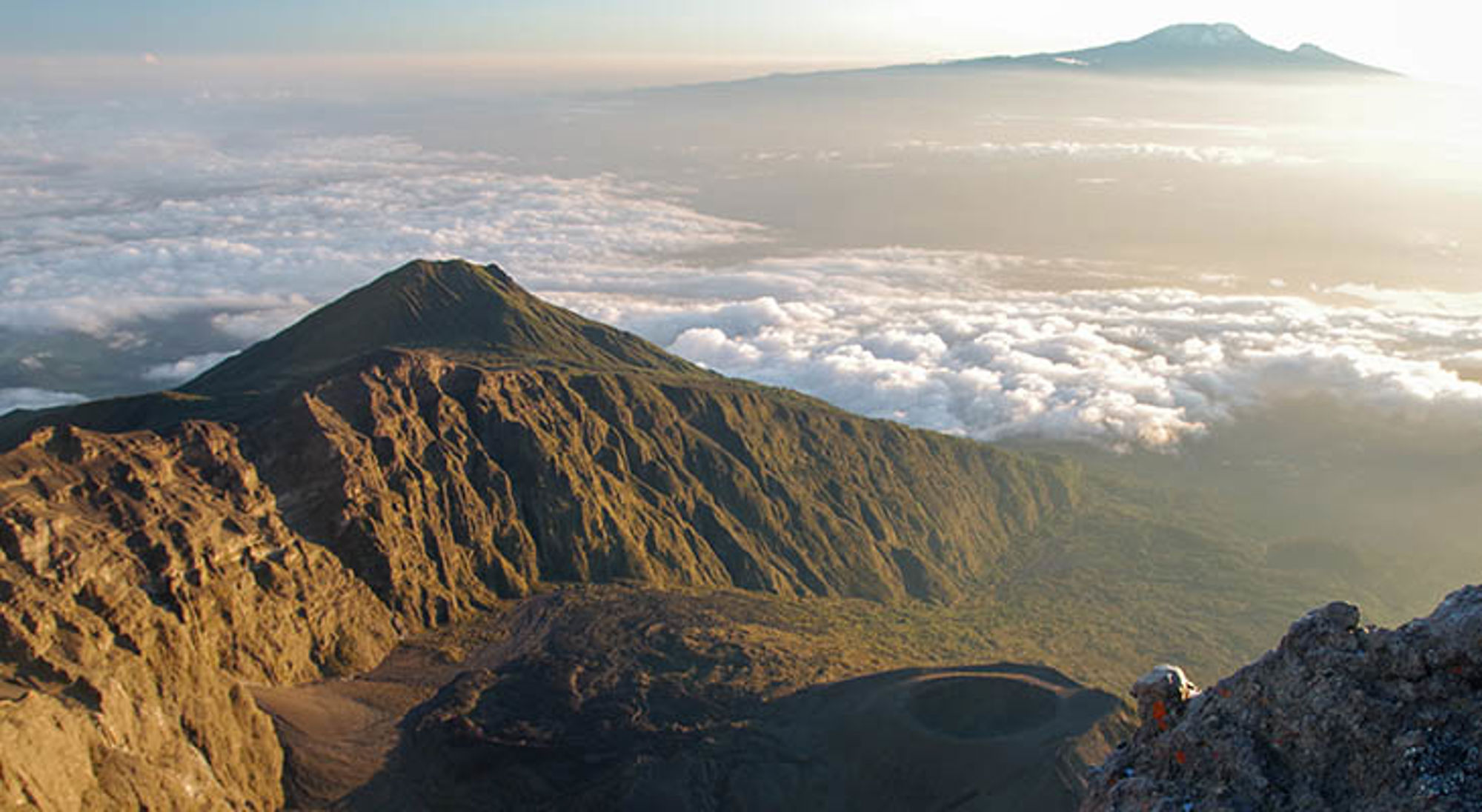 Uitzicht op Mount Meru Uitzicht vanaf de Kilimanjaro over de vulkanische bergkam en een zee van wolken bij zonsopgang.