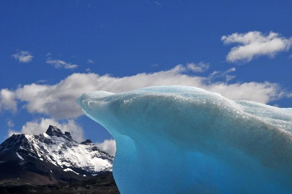 Blauwe ijsberg met besneeuwde bergtoppen onder een heldere lucht in Patagonië.