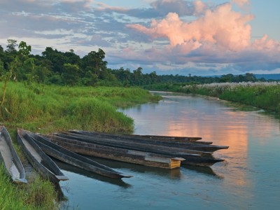 Houten kano’s aan de oever van een rustige rivier bij zonsondergang.