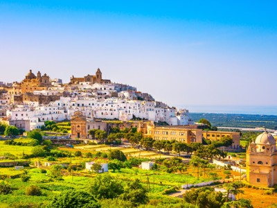 Witte huizen van Ostuni op een heuvel in Puglia, met kerkkoepels en groen landschap onder een blauwe lucht.