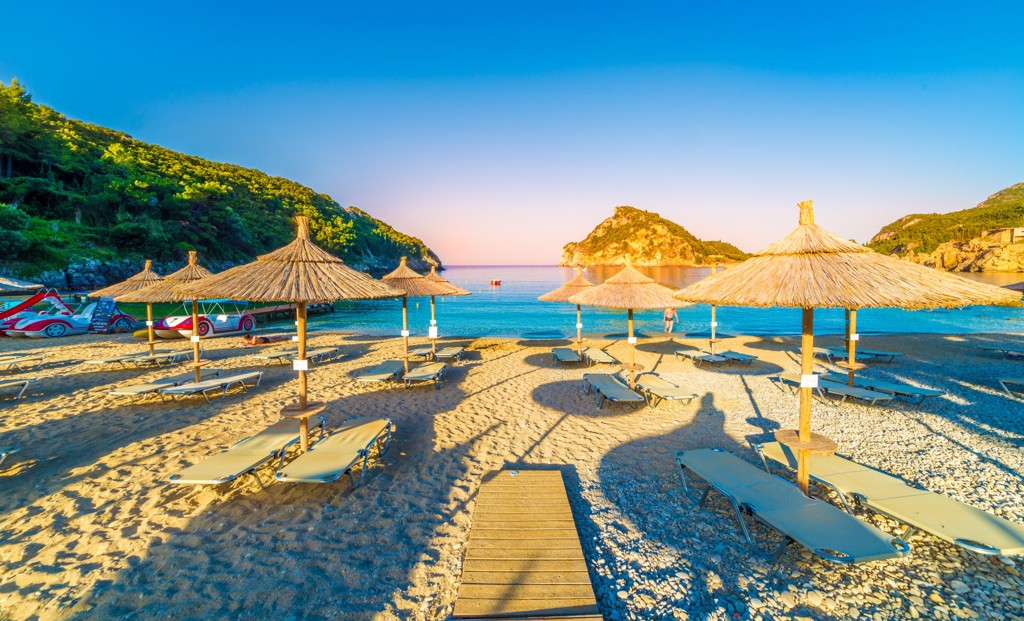 Strand in Noord-Griekenland met rieten parasols, ligbedden en helderblauw water in een baai.
