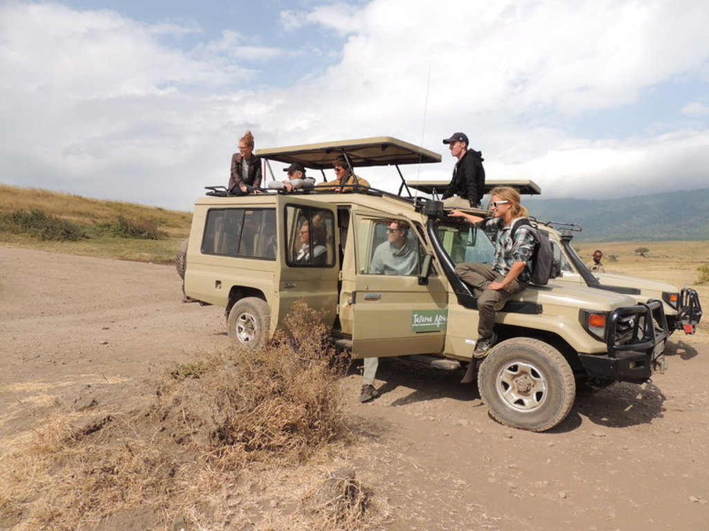 Safari-jeep met reizigers tijdens groepsrondreis Kenia en Tanzania, met uitzicht op savanne en bergen.