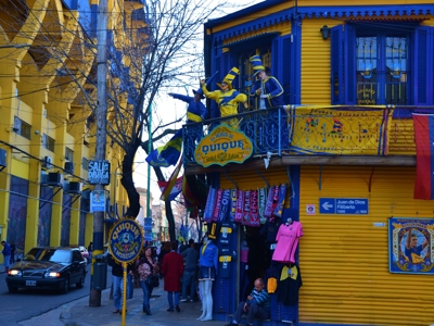 Kleurrijke straat in La Boca, Buenos Aires, met gele gebouwen, balkon en straatartiesten in geel-blauw.