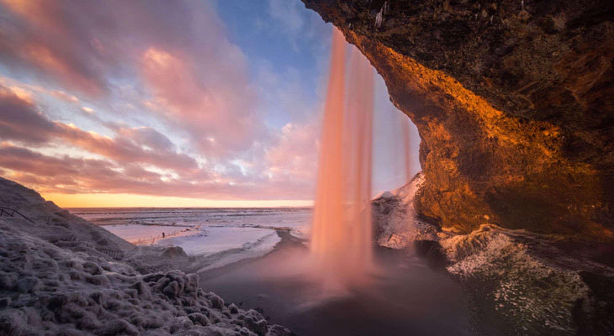 Waterval Seljalandsfoss in IJsland bij zonsondergang, gezien vanaf achter de waterval.