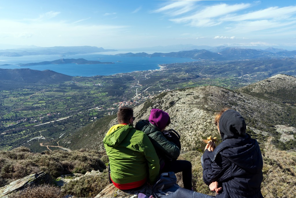 Wandelaars pauzeren op een bergtop op Evia met uitzicht op zee, eilanden en groene valleien in Griekenland.