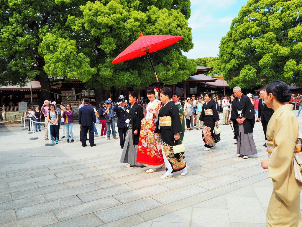 Traditionele Japanse bruiloftsstoet bij een tempel, met bruid in kimono onder een rode parasol.