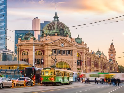 Flinders Street Station in Melbourne met groene tram en stadse skyline bij zonsondergang.