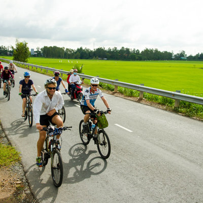 Groep fietsers tijdens fietsvakantie Vietnam, Cambodja & Thailand langs groene rijstvelden.