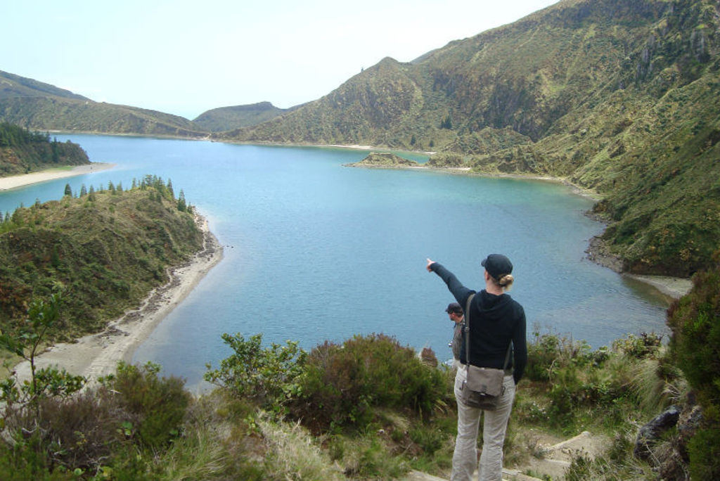 Wandelaar wijst uit over een kratermeer op São Miguel, Azoren, tijdens een wandelvakantie.