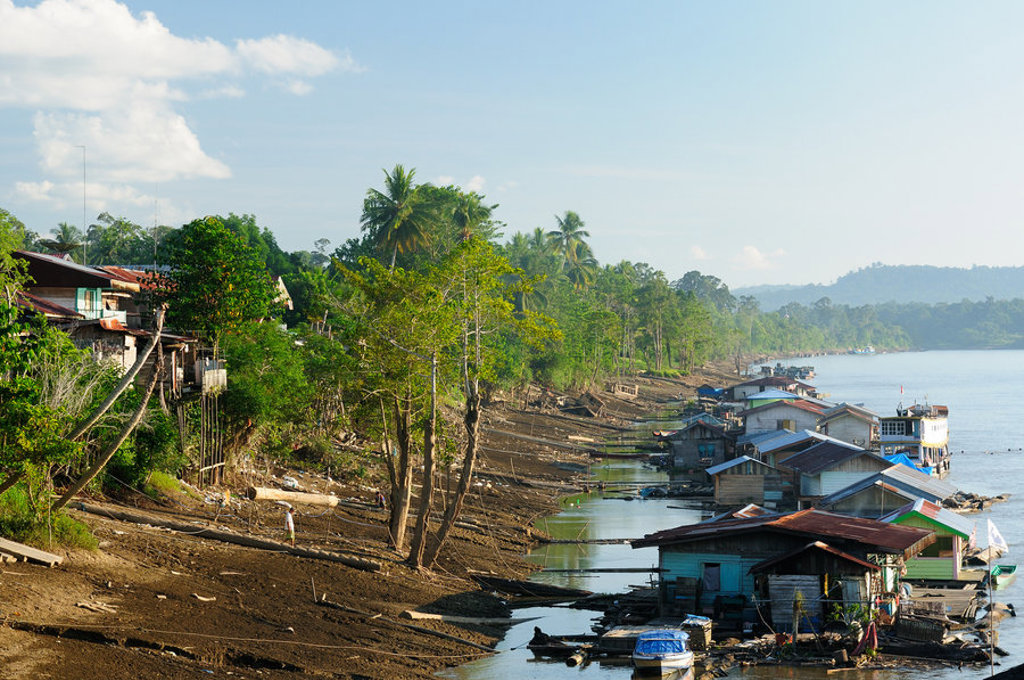 Huizen langs de rivier in Kalimantan, Indonesië, omgeven door groen.