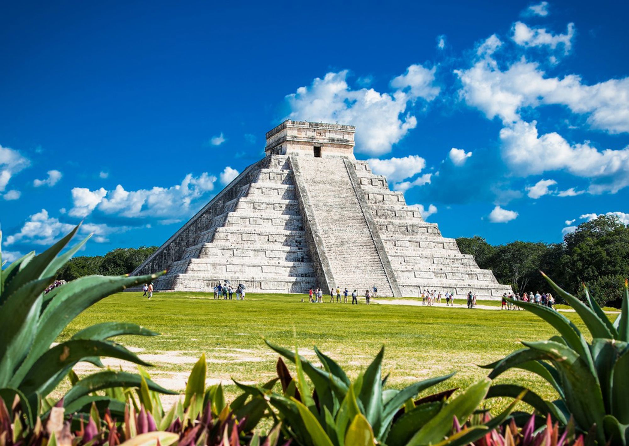 Piramide El Castillo (Chichén Itzá) in Mexico met bezoekers op het grasveld onder een blauwe lucht.