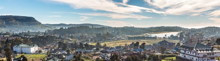 Panorama over Nuwara Eliya met heuvels, akkers, huizen en het Gregory Lake onder een blauwe lucht.