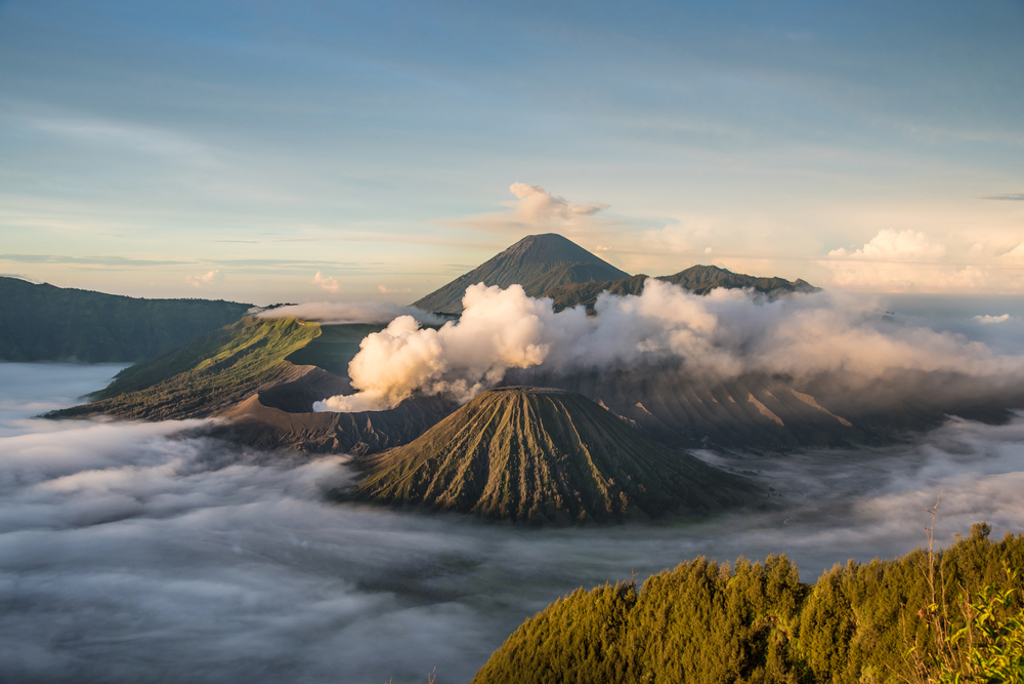 Vulkanlandschap op Java met rookpluimen en wolken boven de krater, tijdens familiereis Java & Bali.