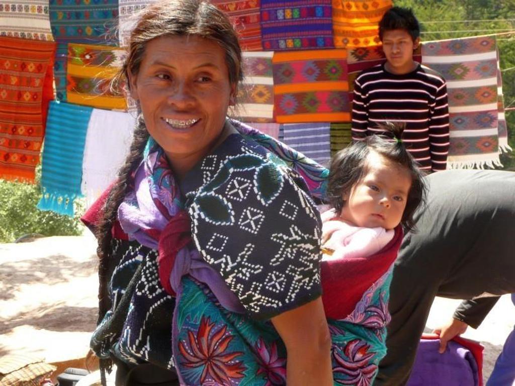 Vrouw met baby op de rug voor kleurrijke textielmarkt in Guatemala tijdens familiereis Guatemala en Belize.