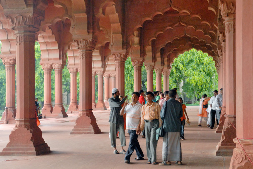 Bezoekers in een zuilengalerij met roodstenen bogen bij een historisch monument in Noord-India.