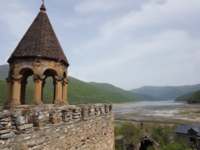 Kerk met stenen toren bij het Zhinvali-stuwmeer in Georgië, met uitzicht op groene bergen.