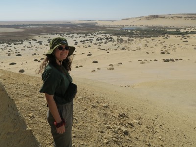 Reiziger met hoed kijkt uit over zandduinen en oase in de Egyptische woestijn tijdens Route Egypte dag 6.