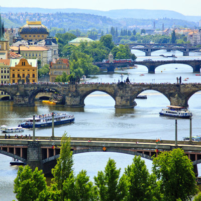 Uitzicht op de Karelsbrug over de Moldau in Praag, met rondvaartboten en de skyline van de stad.