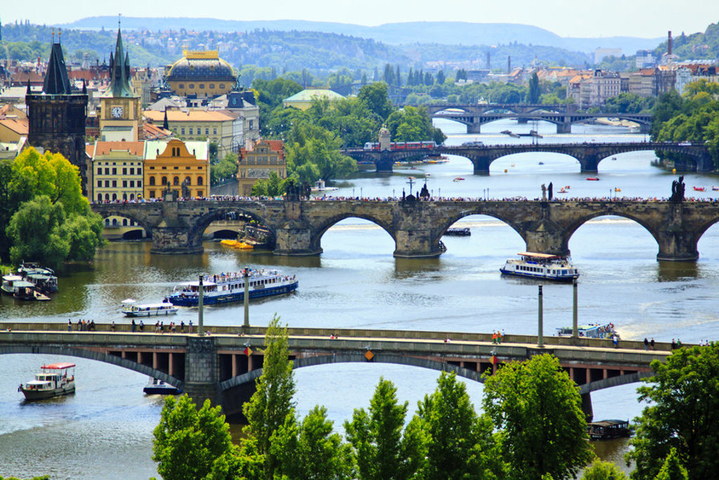 Uitzicht op de Karelsbrug over de Moldau in Praag, met rondvaartboten en de skyline van de stad.