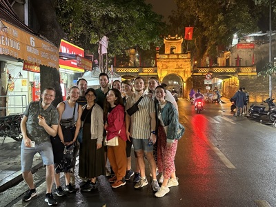 Groepsfoto van reizigers bij de verlichte toegangspoort van de oude stad in Hanoi, Vietnam, in de avond.