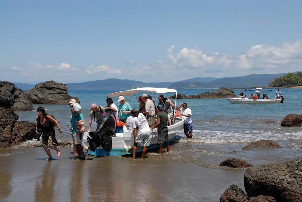 Reizigers stappen uit een boot aan een rotsachtig strand in Costa Rica tijdens een groepsrondreis.