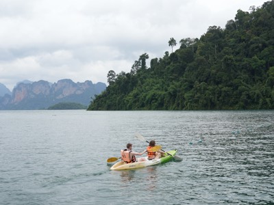 Twee reizigers kajakken op een meer met groene jungleheuvels en kalkstenen bergen in Thailand.