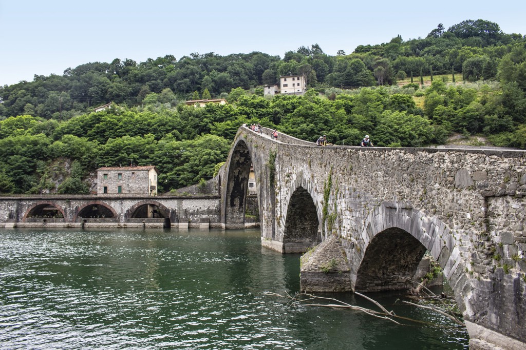 Fietsers op een historische stenen boogbrug over een rivier in Toscane, Italië.