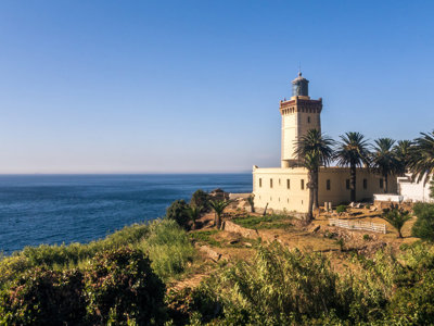 Vuurtoren op een klif aan de Atlantische kust van Marokko, omringd door palmbomen.