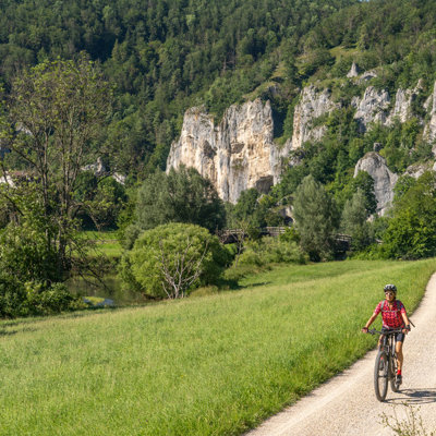 Fietser op het Donauradweg-fietspad langs de Donau, met groene heuvels en rotswanden op de achtergrond.