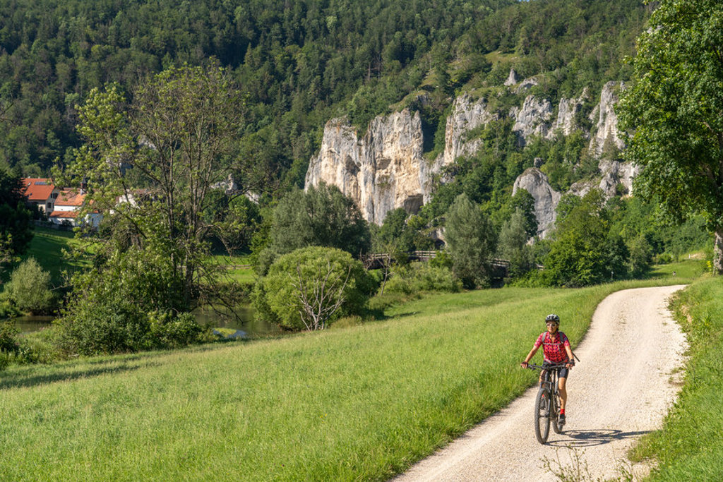 Fietser op het Donauradweg-fietspad langs de Donau, met groene heuvels en rotswanden op de achtergrond.