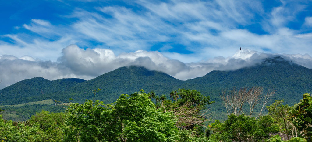 Groene vulkanen en regenwoud in Costa Rica onder een blauwe lucht met wolken.