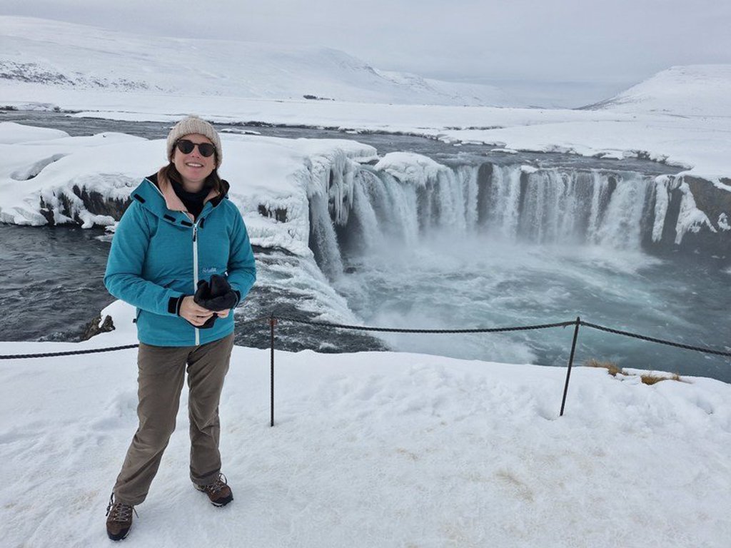 Reiziger in winterkleding bij een besneeuwde waterval in Noord-IJsland tijdens een groepsrondreis.